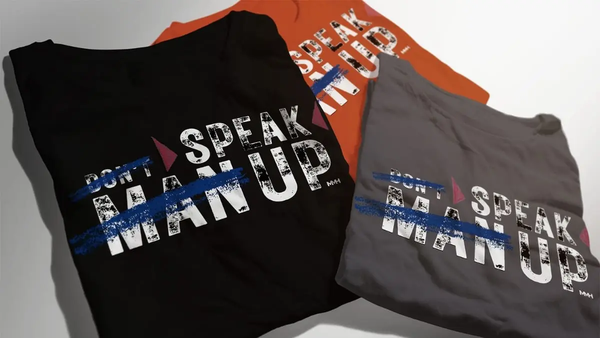 Folded t-shirts featuring the “Don’t Man Up, Speak Up” design from MMH Men’s Mental Health merch range.